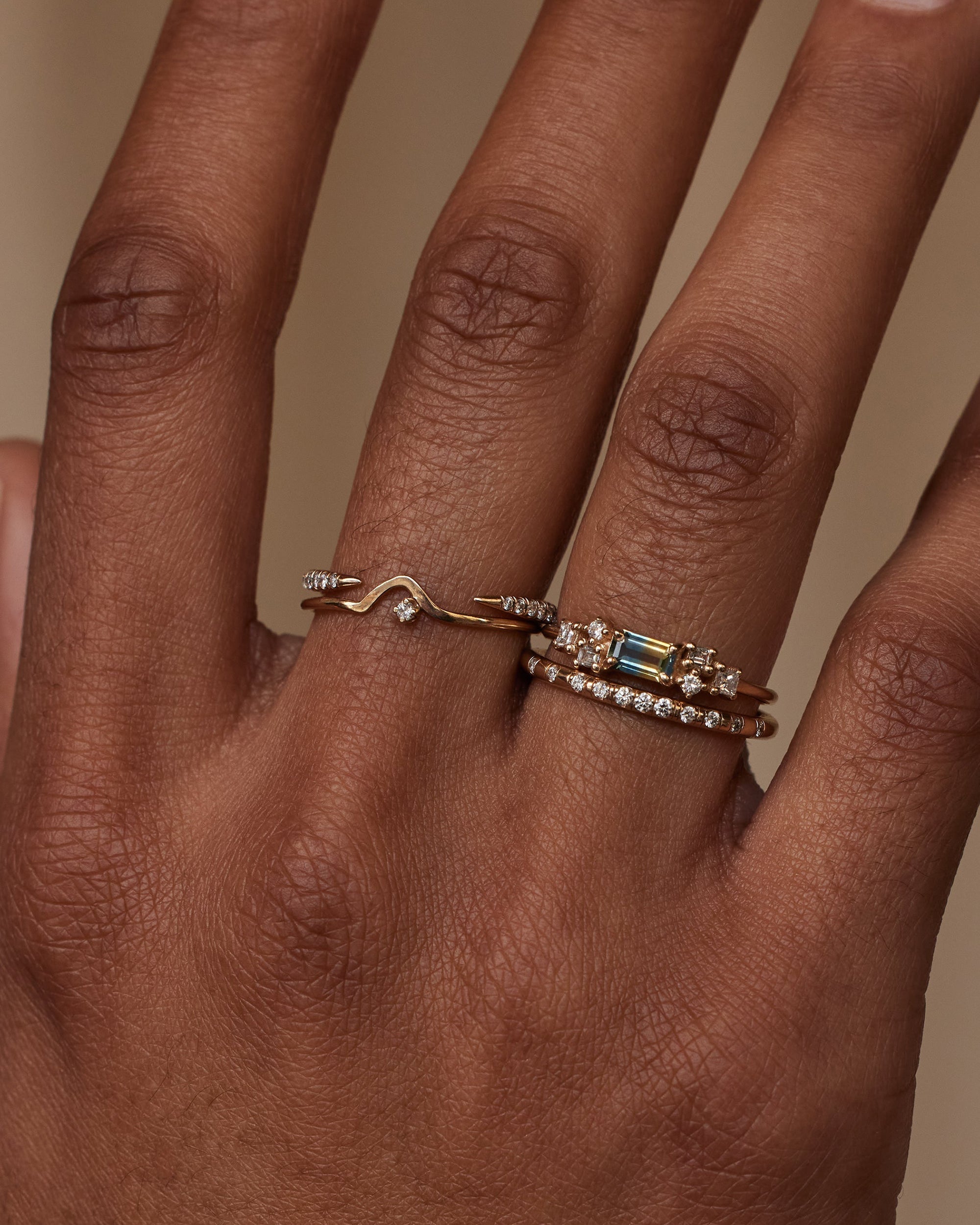 [lifestyle]Hand wearing two gold rings with gemstones on a neutral background