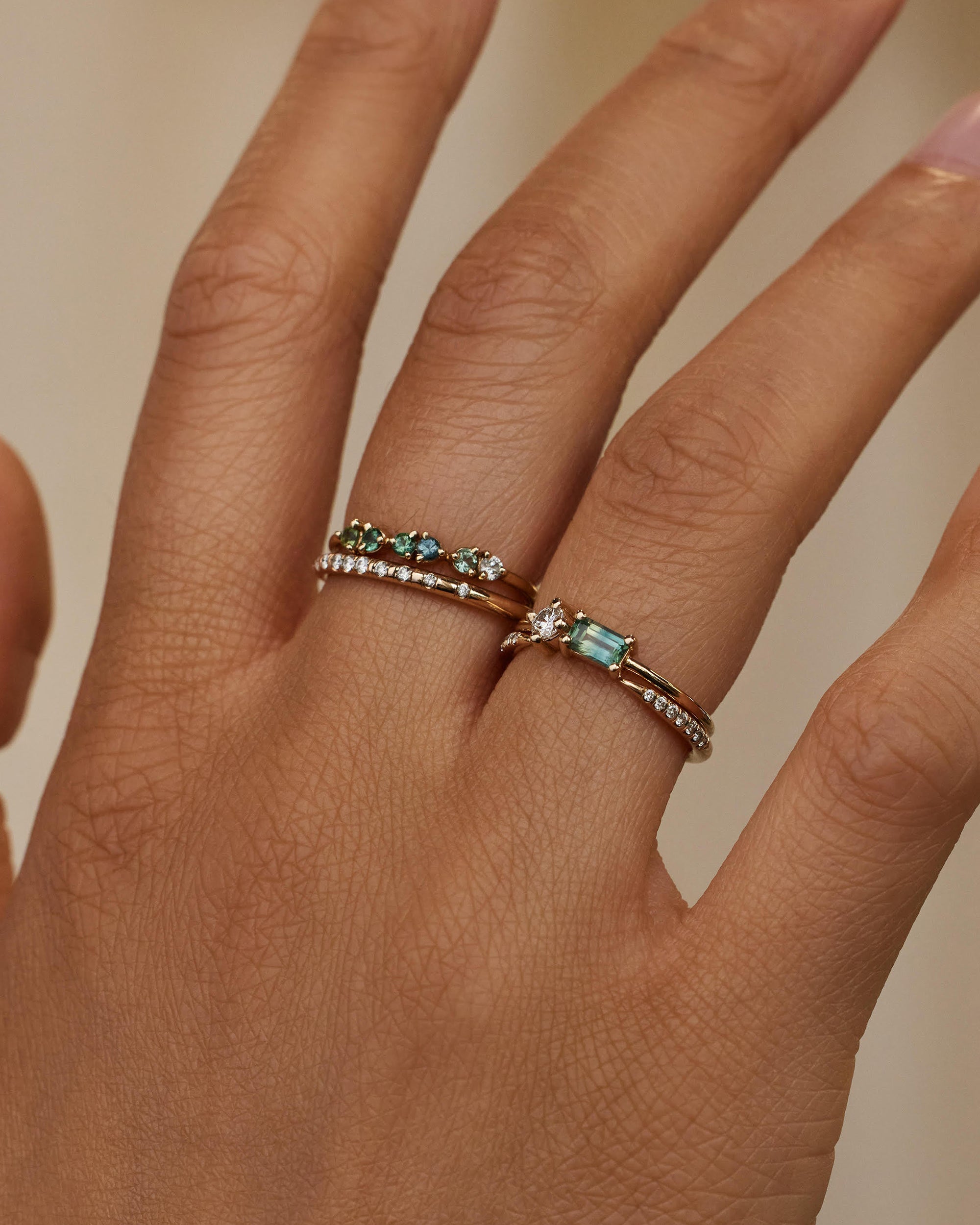 [lifestyle]Hand wearing two rings with gemstones on a neutral background