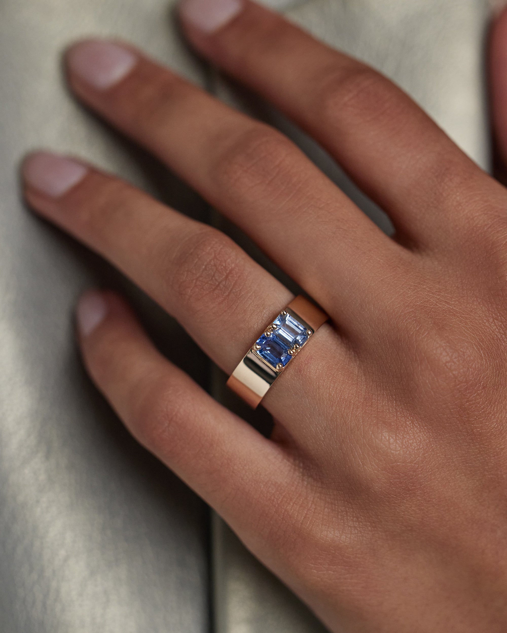 [lifestyle]Gold ring with a blue gemstone on a hand against a neutral background