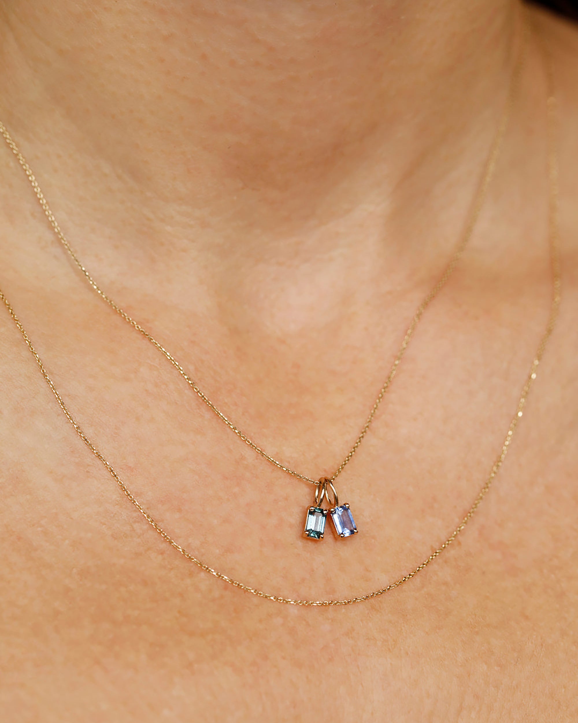 [lifestyle]Gold necklace with a small pendant featuring blue gemstones on a person's neck.